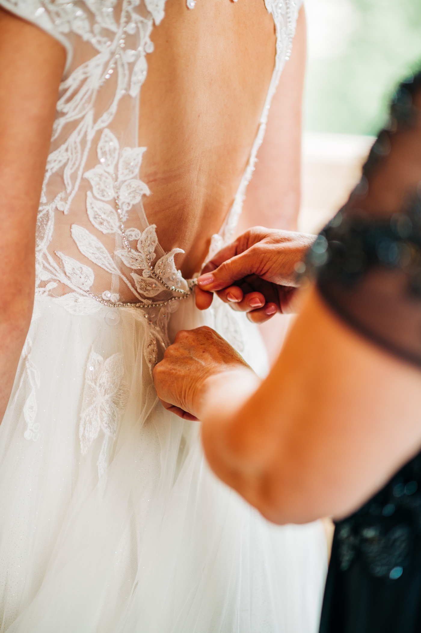 Mother of the bride helping bride into lace wedding gown