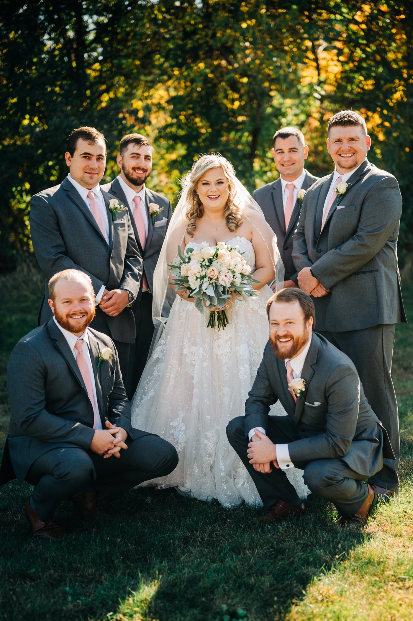 Bride with groomsmen who are wearing grey suits and blush ties