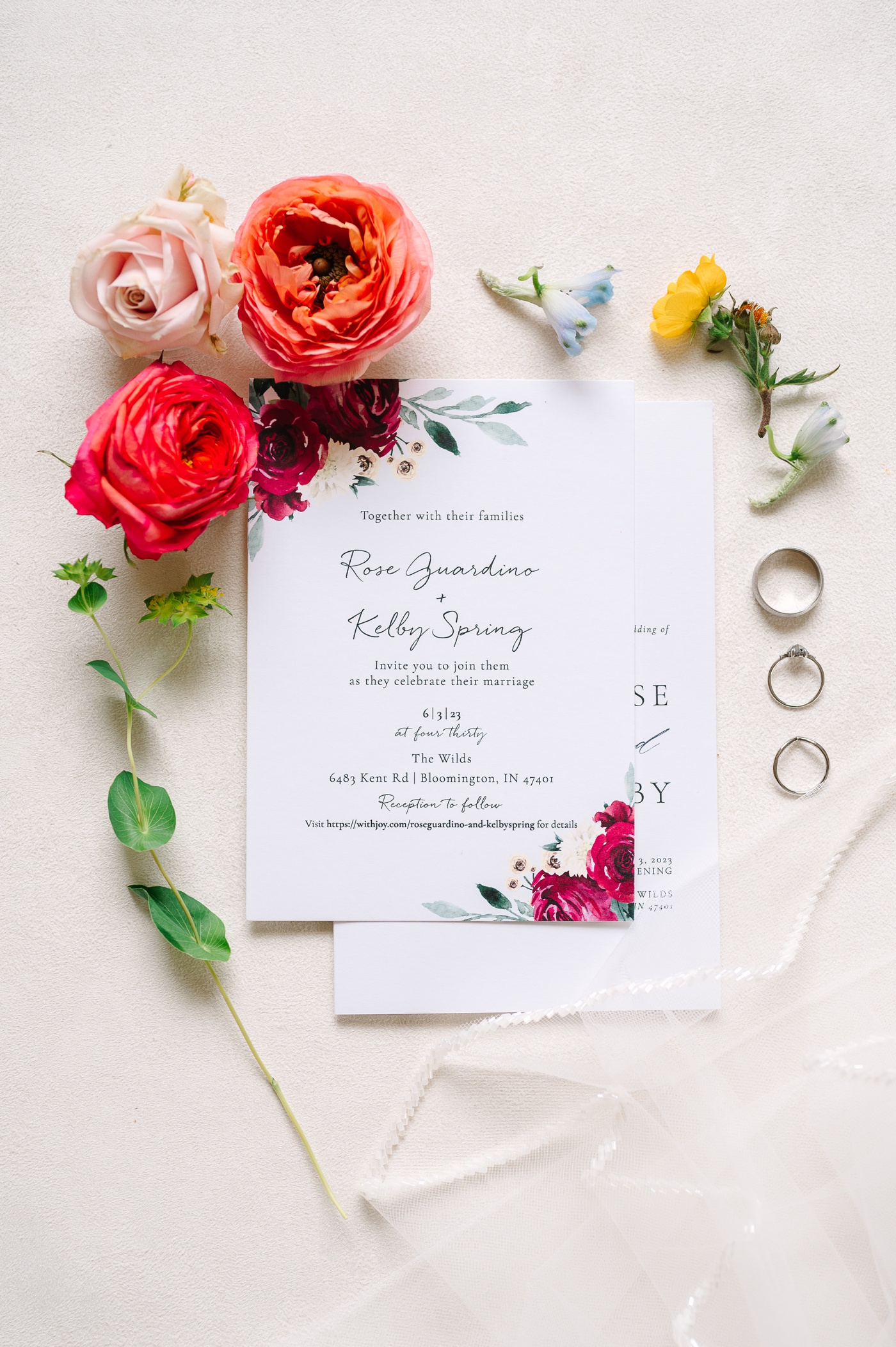 Wedding flat lay with a botanical wedding invitation, rings, and colorful flowers