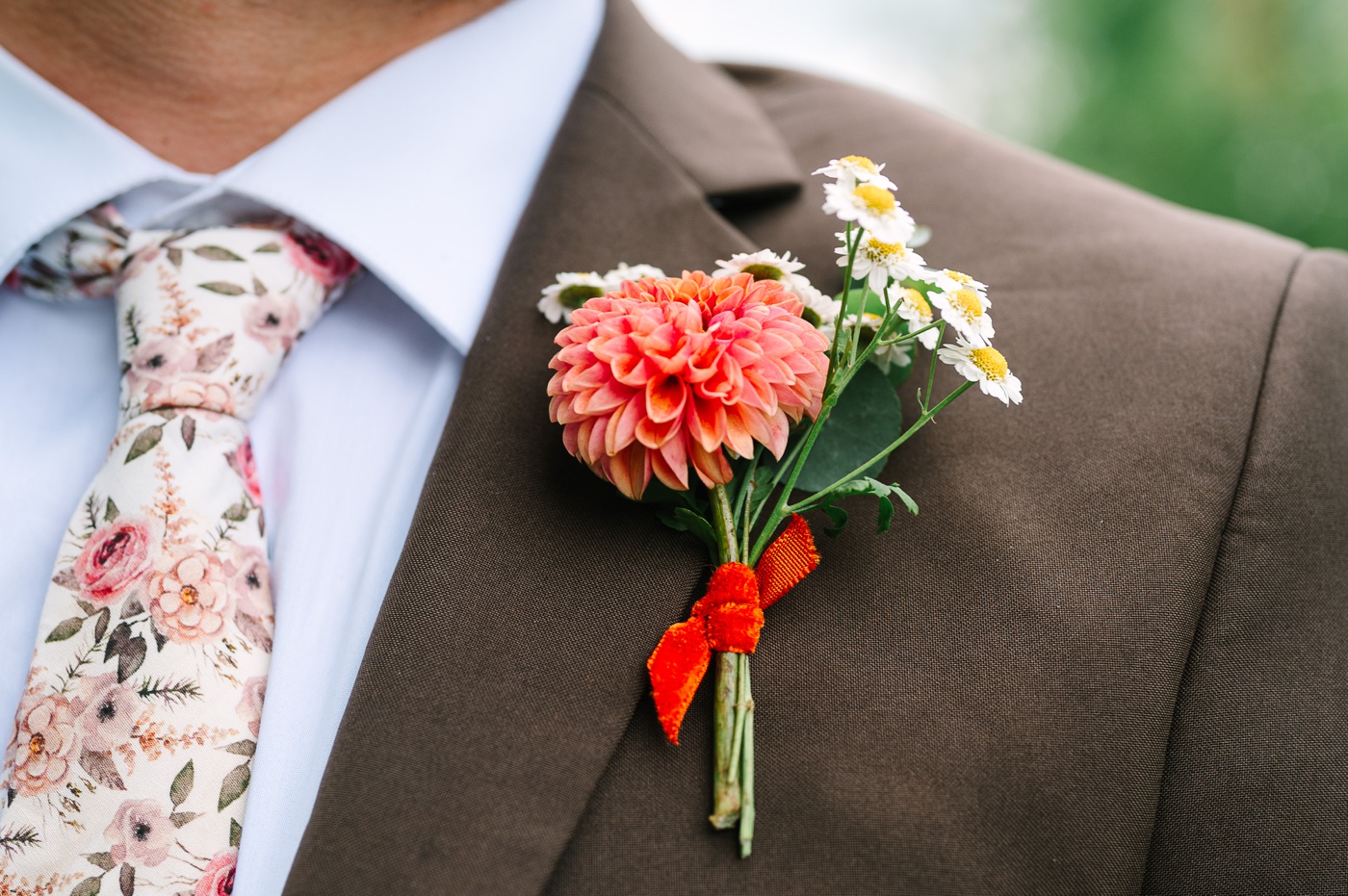 Spring wedding boutonniere filled with an orange dahlia and miniature daisies