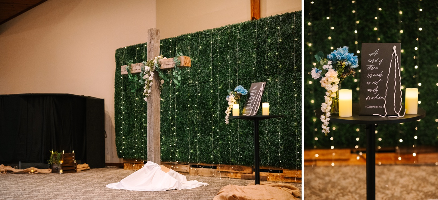 A wooden cross in front of a grass wall with hanging lights at an Indiana wedding