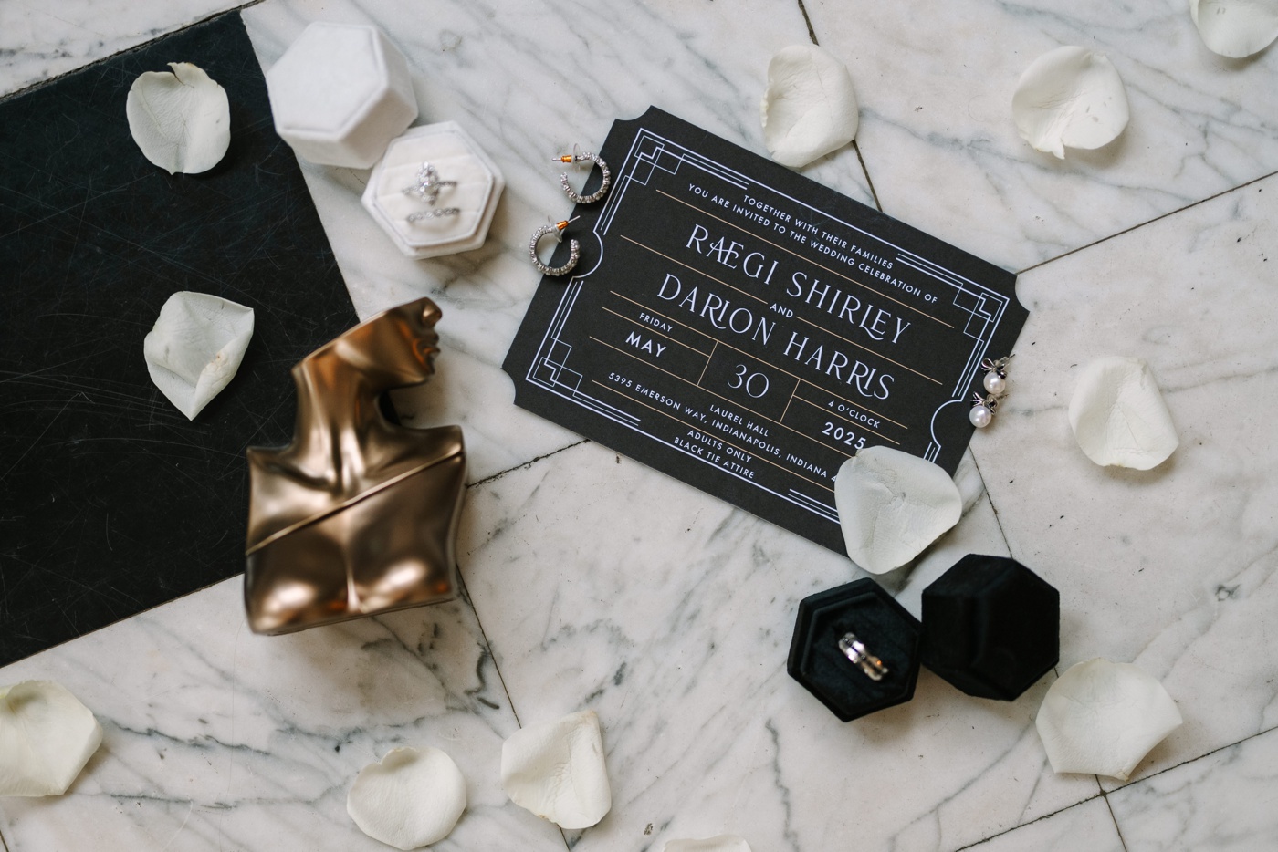 Flatlay of a black Art Deco wedding invitation and a golden female bust figurine